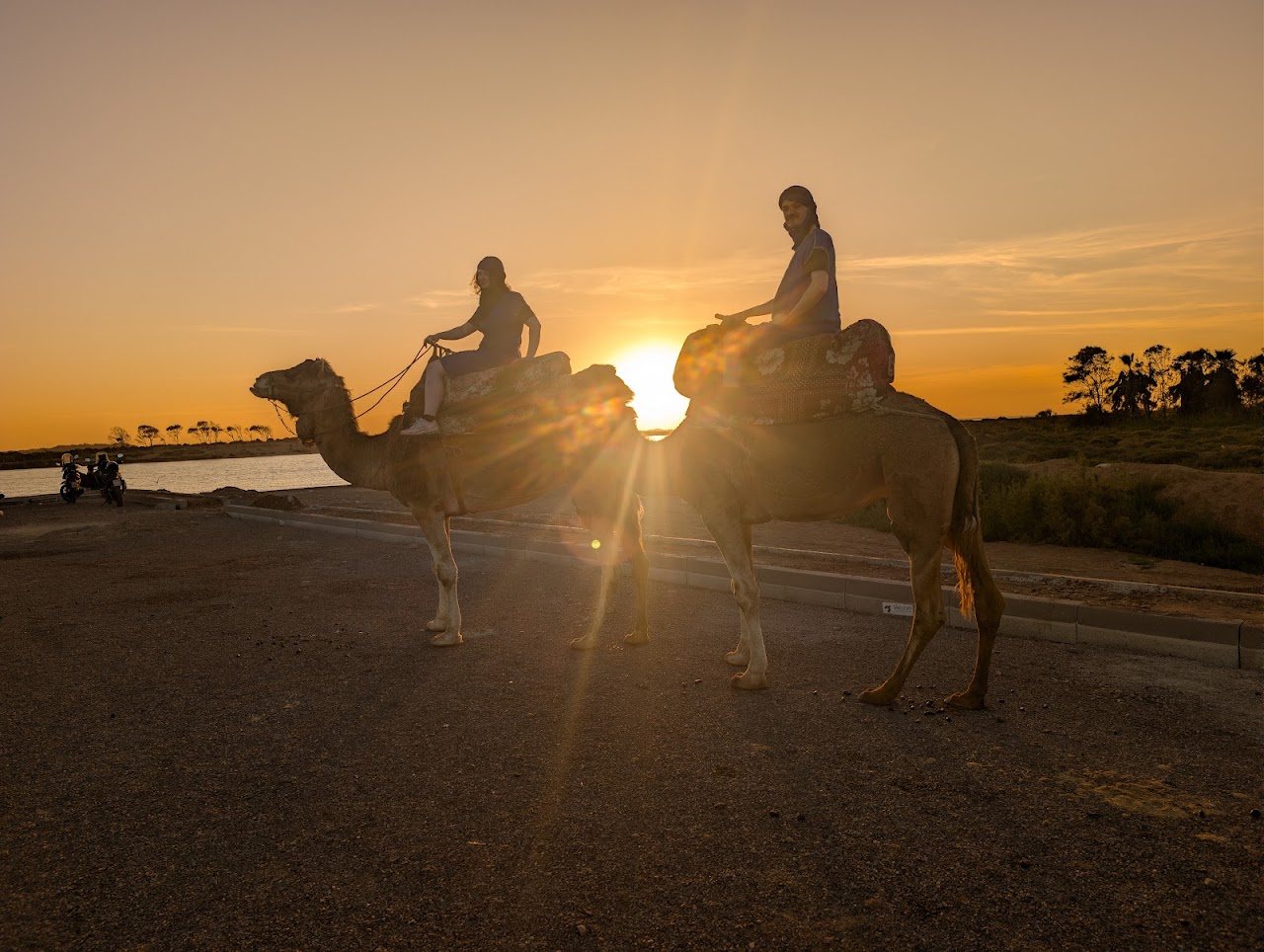 Deux cavaliers à dos de dromadaire en silhouette devant le soleil couchant près d’Agadir