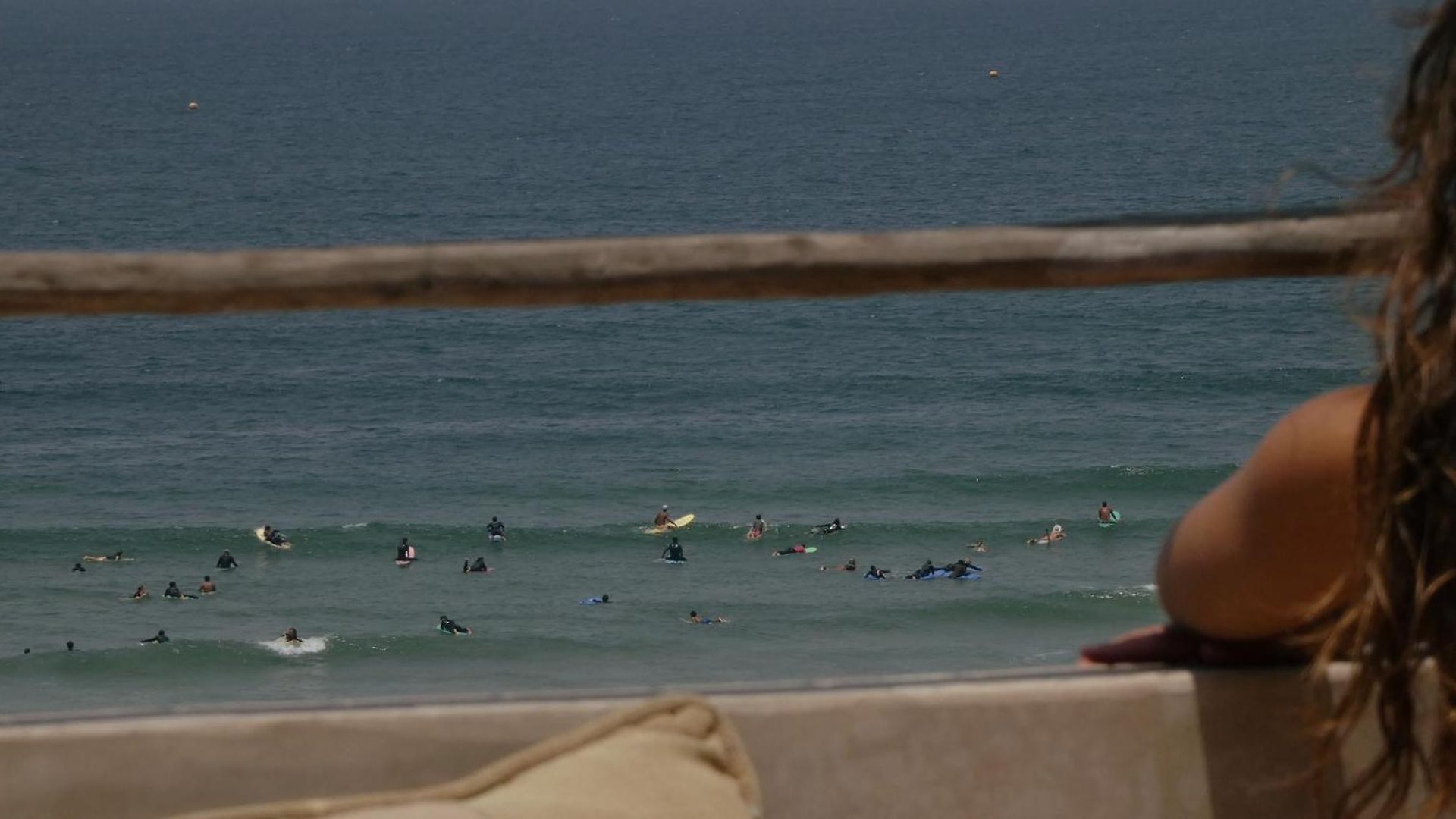 Guest at the rooftop rail watching surfers in the water at Anza