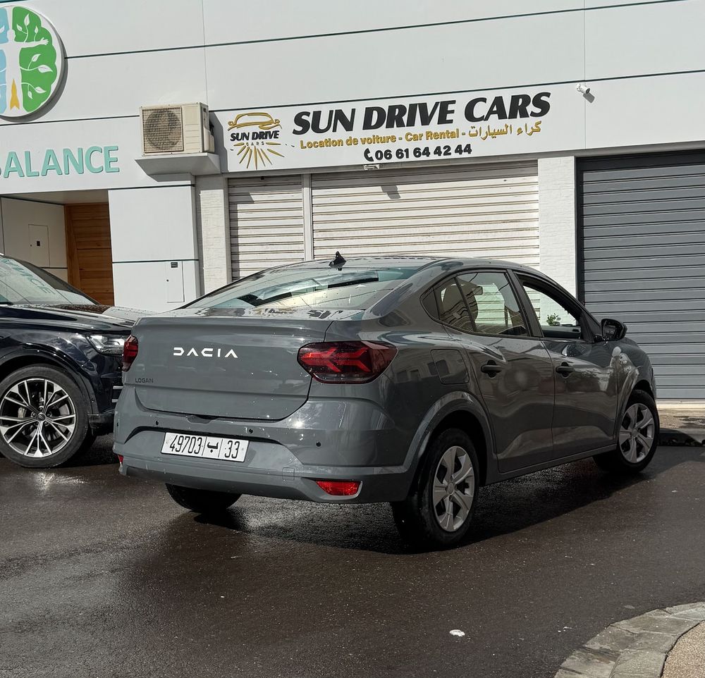 Sun Drive Cars storefront in Talborjt with its trilingual sign and a grey Dacia Logan parked in front